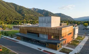 Modern building with wood siding and orange brick, set against a backdrop of a lush green mountain range.