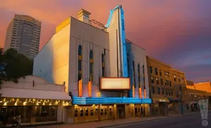 An old-fashioned theater with neon blue and orange lights glows at sunset.