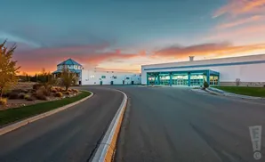 A modern building with blue accents at sunset, with a road curving towards it.