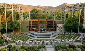 An outdoor amphitheater stage with seating, set against a backdrop of hills and trees.