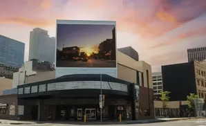 A movie theater marquee displays a sunset over a city street, with modern buildings in the background.