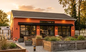 An orange building with large windows and an outdoor seating area with planters.