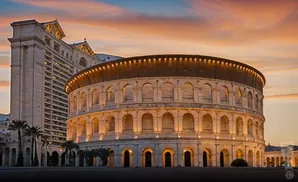 A Roman-style amphitheater and hotel at sunset with a colorful sky.