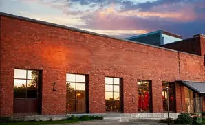 Exterior of a red brick building with large windows reflecting a sunset sky.