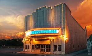 Art deco theater facade with a neon marquee glows under a dramatic orange sunset sky.