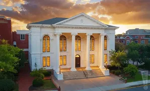 White classical building with columns and arched windows at sunset.