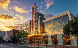 A theater marquee glows under a dramatic sunset sky with clouds reflecting in the building's windows.