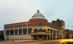 A large, domed building with a marquis in front, illuminated by streetlights on a hazy day.