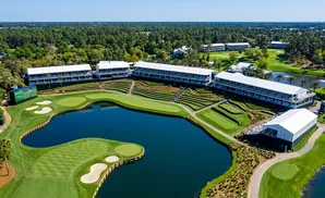 Aerial view of a golf course with a large lake, tiered seating, and white tents.