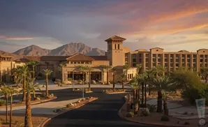 A resort building with palm trees and mountains under a sunset sky.