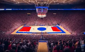 Basketball game in a packed arena with red and blue court markings and a large scoreboard.