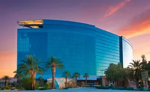 A modern, blue-glass hotel with palm trees in front against a vibrant sunset sky.