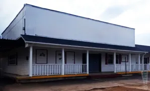 A white, long, single-story building with a covered porch and a large white sign above.