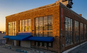 An old brick industrial building with large, grid-paned windows at sunset.