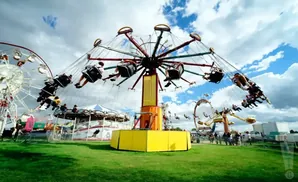 A swing ride spins with people on it at a carnival with a Ferris wheel in the background.