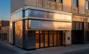 Modern building entrance with reflective metallic facade and large glass doors, bathed in golden sunset light.