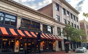 Street view of buildings with striped awnings, large windows, and a parked silver sedan.