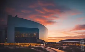 Modern stadium at sunset with dramatic clouds and glowing lights.