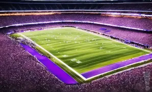 An aerial view of a brightly lit football stadium at night with a large crowd of spectators in purple seats.