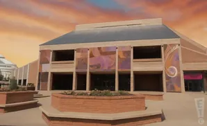 An abstract mural adorns the brick facade of a modern building under a dramatic orange sky.