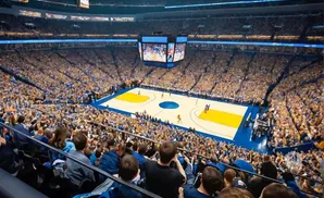 A basketball game in a packed arena, with fans in yellow and blue cheering from the stands.