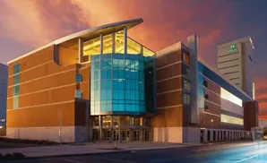 A modern building with orange brick and blue glass, illuminated by a sunset.