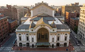 An aerial view of a grand, ornate theater with copper domes, golden detailing, and a large arched entryway.