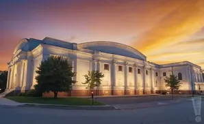 Grand white building with columns under a vibrant orange and purple sunset sky.