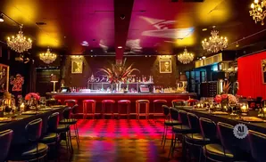 A glamorous bar with chandeliers, red bar stools, and a long table set for dining.