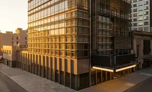 Golden hour light reflects off the glass facade of a modern, multi-story building in an urban setting.