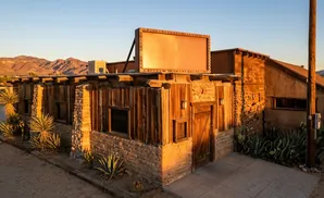 Rustic desert building with wooden walls, stone foundation, and a large blank marquee under a clear sky.