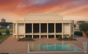 Modern building with columns, large windows, a reflecting pool, and a sunset sky.