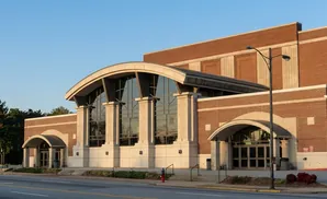 Modern brick building with large arched windows and entrances, a street and light post in the foreground.