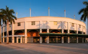 A curved, white building with arched entrances and palm trees under a clear blue sky.