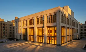 A modern building with stone facade and large windows glows in warm sunset light.