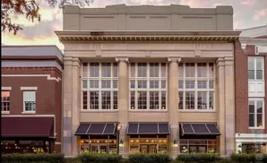 A grand building with large windows and columns, flanked by brick buildings.