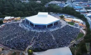 Aerial view of an outdoor amphitheater with a large white-roofed stage and a full audience in tiered seating.