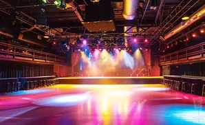 An empty concert venue with colorful stage lighting and scattered stools.