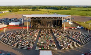 Aerial view of an outdoor concert with a band performing on stage and a large audience seated in an amphitheater.