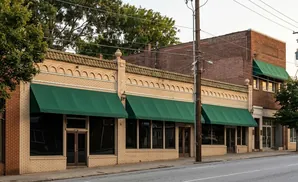 A row of brick buildings with green awnings and large windows line a street.