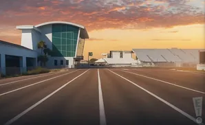 A modern building with a curved glass facade faces a track under a vibrant sunset sky.