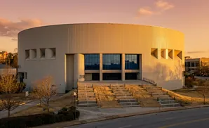 A circular building with large windows and tiered stairs leading up to its entrance during sunset.
