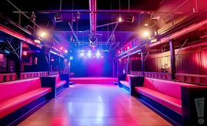 A dimly lit nightclub stage with a bright purple and blue spotlight, red seating, and a disco ball.