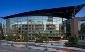Modern glass and brick building with a large curved glass facade reflecting city lights and a dark sky.