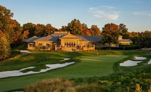 A golf course clubhouse surrounded by autumn trees at sunset.