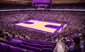 A high-angle view of a crowded basketball arena with purple seats and a cream-colored court.