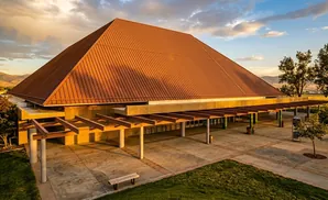 A modern building with a large, copper-colored pyramidal roof and covered walkway.
