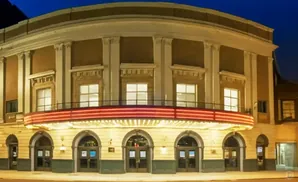 Exterior of a curved, brick theater at night with a glowing marquee and arched doorways.