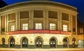 A grand theater facade at night, with arched doorways and a brightly lit marquee.