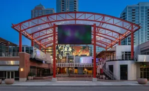 Modern outdoor plaza with red-framed canopy, large screen, and surrounding buildings.